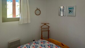 Ett sovrum med en säng, ett fönster med gardiner, en spegel som hänger på väggen och två inramade tavlor.