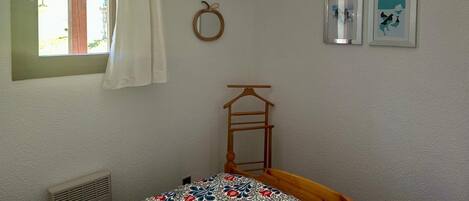 A bedroom with a bed, a window with curtains, a wall-mounted mirror, and two framed pictures.