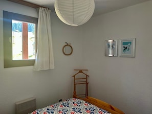 A bedroom with a bed, a window with curtains, a wall-mounted mirror, and two framed pictures. - Appartement au pied des pistes Chez NEll (Molines-en-Queyras)