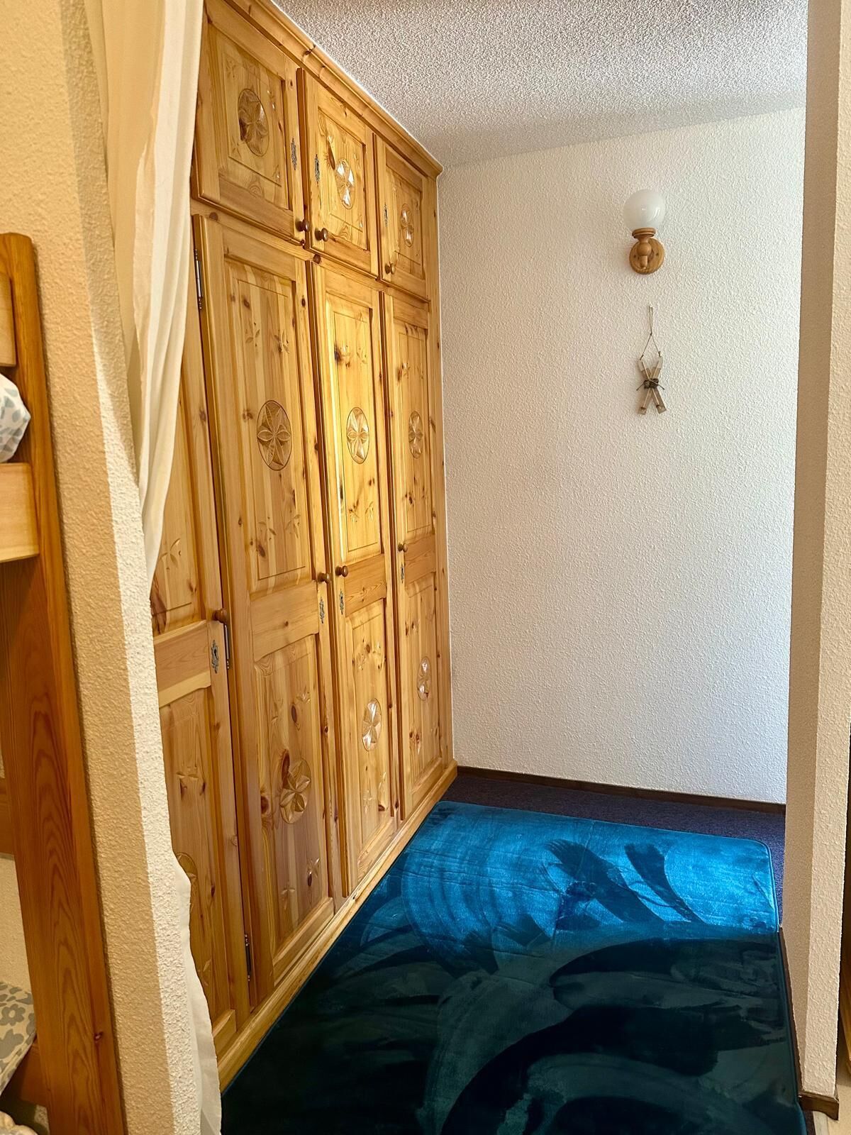 Une pièce avec une armoire en bois, un tapis à motifs bleus et un luminaire fixé au mur.