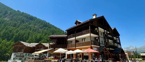 A multi-story wooden building with outdoor seating and a mountain backdrop.