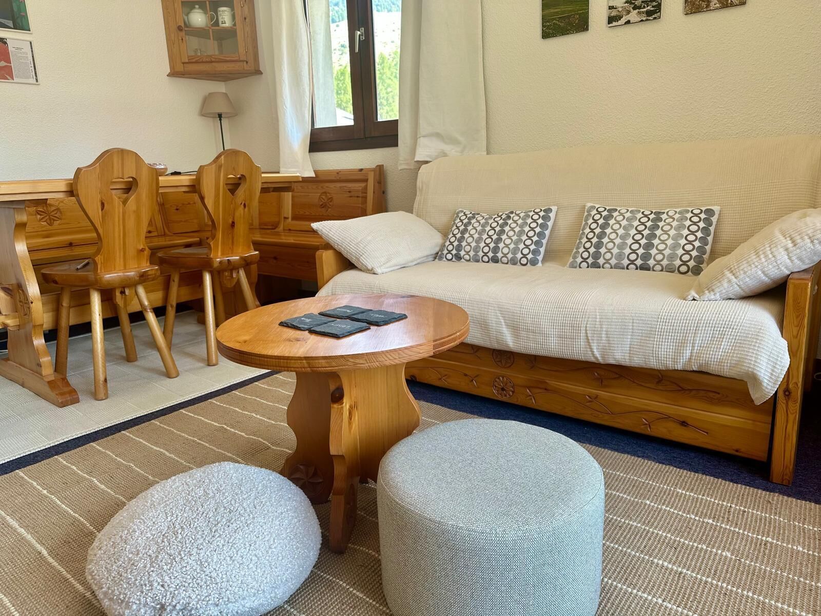 A cozy living area with a sofa, wooden chairs, a round wooden table, and two ottomans.