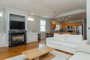A modern living room with a fireplace, a flat-screen TV, and a white sofa. - Spacious Coastal Retreat (Kure Beach)