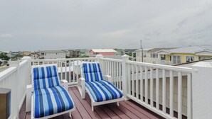 A balcony with two striped lounge chairs and a white railing overlooking a residential area.