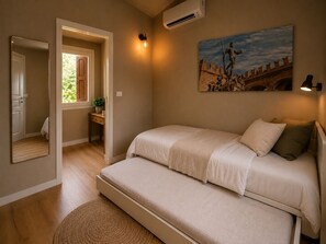A bedroom with a bed, a bedside table, a mirror, an air conditioning unit, and a painting on the wall.