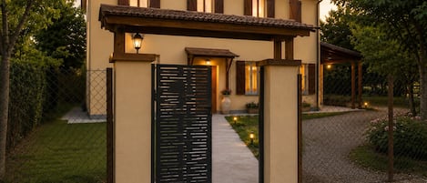 A two-story building with a tiled roof, a gated entrance, and a pathway leading to the main door.