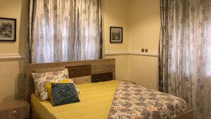 Quarto com cama, cortinas, mesa de cabeceira e duas fotos emolduradas na parede.