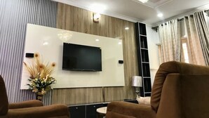 Uma sala de estar moderna com televisão de tela plana presa a uma parede de madeira, um lustre e um sofá.