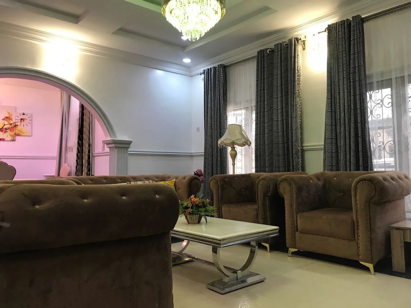 A room with a chandelier, two sofas, a table, and curtains.