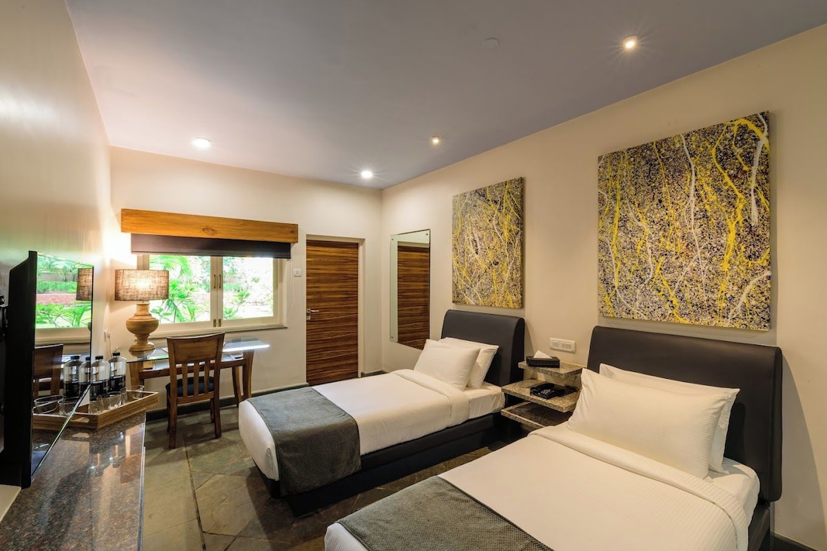 A hotel room with two beds, a desk, a TV, and artwork on the walls.