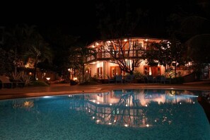 A nighttime view of a hotel with a swimming pool, reflecting the building and surrounding trees. - Argo by Trance (Sancoale)