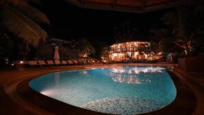 A nighttime view of a swimming pool with lounge chairs and a building in the background. - Argo  by Trance (Sancoale)