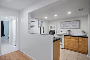 A modern kitchen with a central island, white cabinetry, and a wall-mounted microwave. - Seagate Escape condo w. Beach Access (St Augustine)