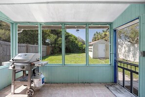A covered patio area with a grill and propane tank, a view of a backyard with a wooden fence and a shed, and a blue door leading outside. - Seagate Escape condo w. Beach Access (St Augustine)