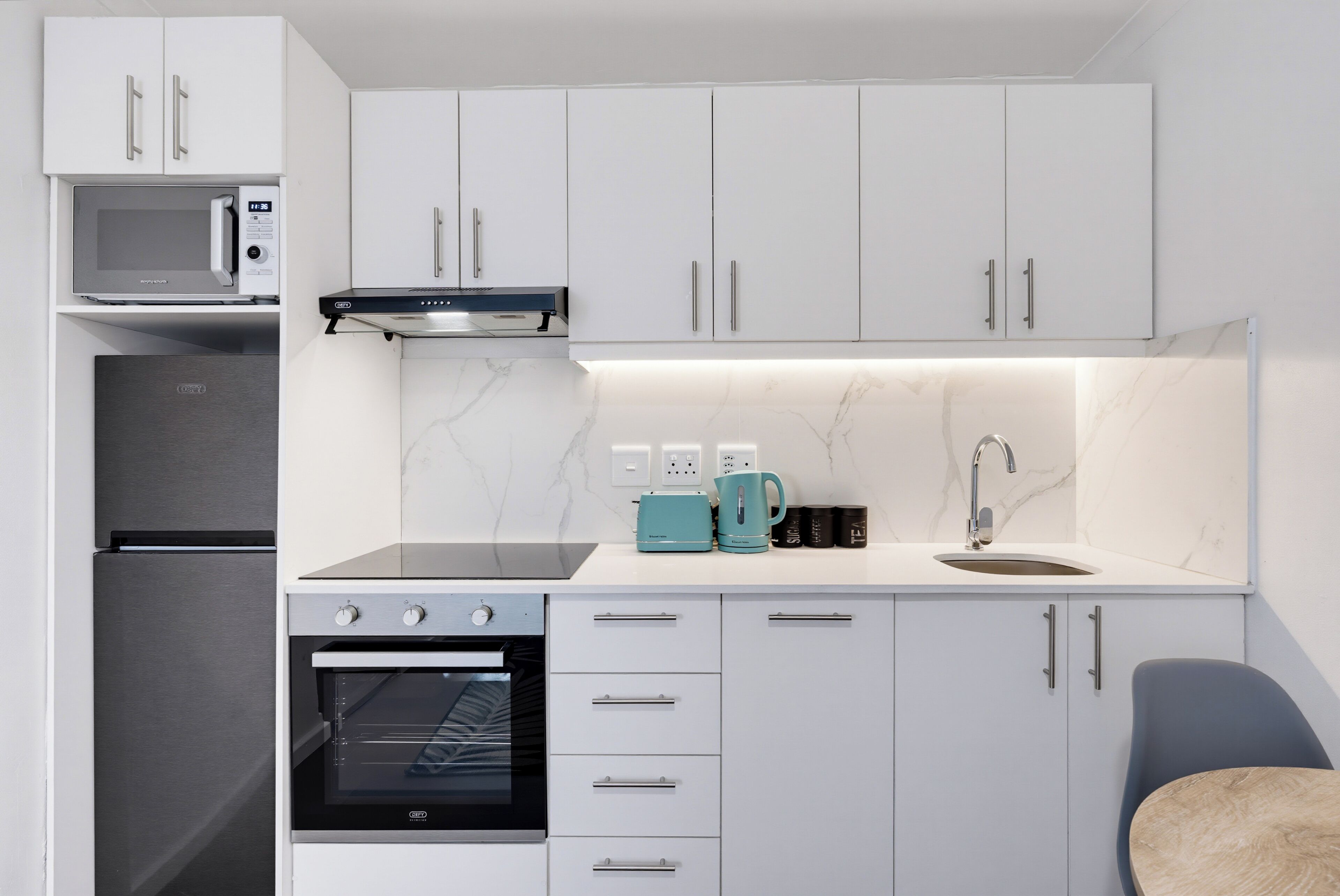 Eine moderne Küche mit weißen Schränken, einem eingebauten Backofen, einer Mikrowelle und einer Kaffeemaschine.