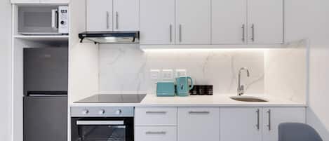 Una cucina moderna con mobili bianchi, forno a incasso, microonde e macchina da caffè.