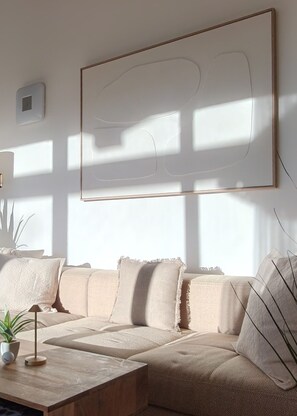 Uma sala de estar moderna com um sofá bege, uma mesa de centro e um grande quadro abstrato na parede.