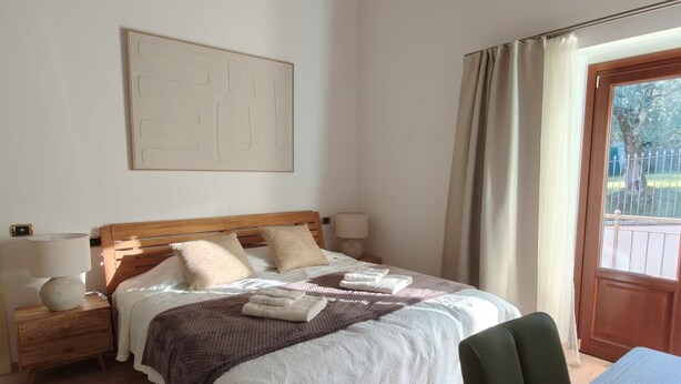 Ein Schlafzimmer mit einem hölzernen Bett, einem Nachttisch, einem Tisch und einem Fenster mit Vorhängen.
