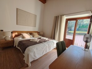 Un dormitorio con cama, mesitas de noche, escritorio, silla, ventana con cortinas y vistas al exterior.