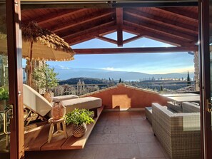 A balcony with a view of a cityscape, a wicker sofa, a small table, and a thatched umbrella. - DELUXE BOGLIACO GOLF APARTMENT MIT 180° - SEEBLICK (Lombardia)