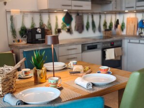 A dining area with a wooden table set for two, a coffee machine, and various kitchen appliances in the background. - DELUXE BOGLIACO GOLF APARTMENT MIT 180° - SEEBLICK (Lombardia)