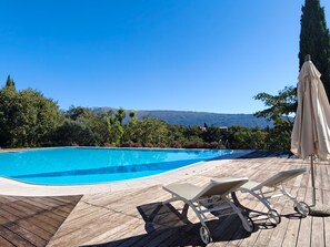 Uma piscina com deck de madeira, espreguiçadeiras e um guarda-sol.