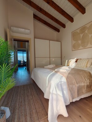 Une chambre avec un grand lit, un plafond en bois et une vue sur l’extérieur par une porte ouverte.
