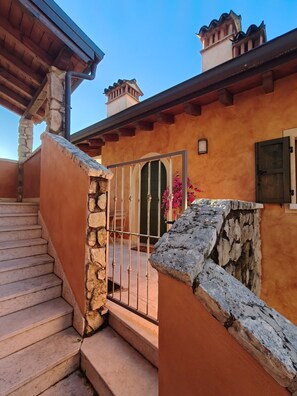 A staircase leading to a stone wall with a metal gate, a door with a window, and a small balcony with a flower pot.