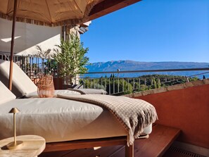Varanda com uma cama, um cesto de vime e vista para as montanhas e o mar.
