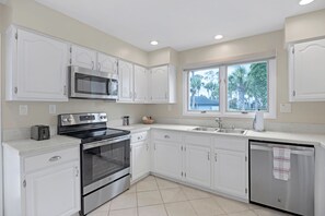 A modern kitchen with white cabinetry, stainless steel appliances, and a window providing a view of the outdoors. - Greenside Getaway - 2BR condo w/ pool access & golf views (Ponte Vedra Beach)