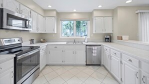 A modern kitchen with white cabinetry, stainless steel appliances, and a window providing natural light. - Greenside Getaway - 2BR condo w/ pool access & golf views (Ponte Vedra Beach)