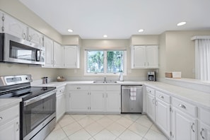 A modern kitchen with white cabinetry, stainless steel appliances, and a window providing natural light. - Greenside Getaway - 2BR condo w/ pool access & golf views (Ponte Vedra Beach)