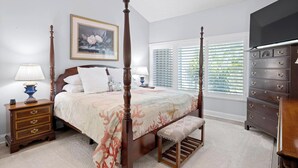 A bedroom with a four-poster bed, a nightstand with a lamp, a dresser with drawers, a bench, and a window with blinds. - The Sawgrass Sanctuary (PONTE VEDRA BEACH)