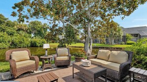 An outdoor seating area with wicker furniture, a lamp, and a view of a pond and greenery. - The Sawgrass Sanctuary (PONTE VEDRA BEACH)