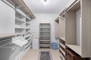 Un dressing accessible sans porte, doté d’étagères ouvertes, d’une tringle à vêtements et d’une petite poubelle.