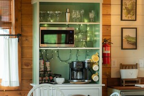 A kitchen with a microwave, coffee maker, and shelves with glassware. - The Farmhouse on Barton | Hocking Hills, Hot Tub (Logan)