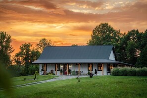 Ein Haus mit geneigtem Dach, einer Veranda mit Sitzgelegenheiten und einem gepflegten Rasen.