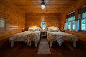 Ein Zimmer mit zwei Betten, einem Deckenventilator, einem Nachttisch und einem Fenster mit Vorhängen.