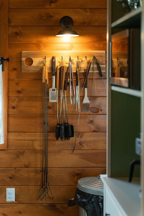 Een keuken met houten wanden, een hanglamp en diverse keukengerei en gereedschappen.