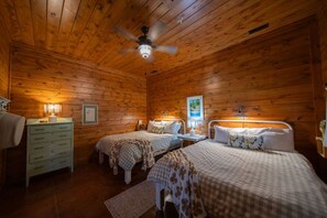 A cabin-style bedroom with two beds, a dresser, and a ceiling fan. - The Farmhouse on Barton | Hocking Hills, Hot Tub (Logan)