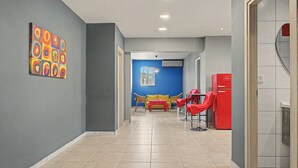 Um corredor com parede azul, geladeira vermelha e sofá amarelo.