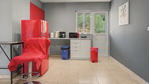 Cozinha compacta com área de refeições, uma cadeira vermelha, uma lixeira azul e uma lixeira vermelha.