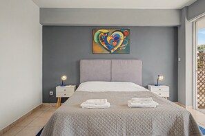 Un dormitorio moderno con una cama grande, dos mesitas de noche, un cuadro abstracto colorido y vistas a través de una ventana.