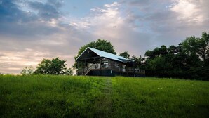 A two-story house with a large deck, surrounded by a grassy field and trees. - The Cottage Barn on Barton | Hocking, Cozy Retreat (Logan)