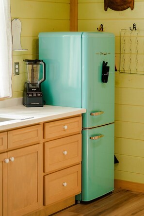 Eine Küche mit einem türkisblauen Kühlschrank, einem Mixer, Holzschränken und einem an der Wand befestigten Regal.