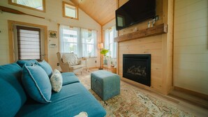 A cozy living room with a sofa, a television, a fireplace, and a window. - The Cottage Barn on Barton | Hocking, Cozy Retreat (Logan)