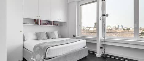 Un dormitorio moderno con cama, estanterías empotradas, un ventanal y vistas a la ciudad.