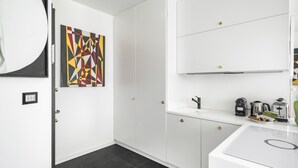 Et moderne køkken med hvide skabe, et sort flisegulv og et geometrisk kunstværk på væggen.