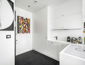 A modern kitchen with white cabinetry, a black tiled floor, and a geometric art piece on the wall. - Porta Nuova 52 Design Apartment R&R (Milan)