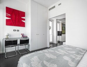 A modern bedroom with a large bed, a desk with two chairs, a red abstract painting, and a view through an open door. - Porta Nuova 52 Design Apartment R&R (Milan)